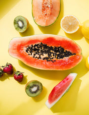 A papaya is surrounded by fruit on yellow background